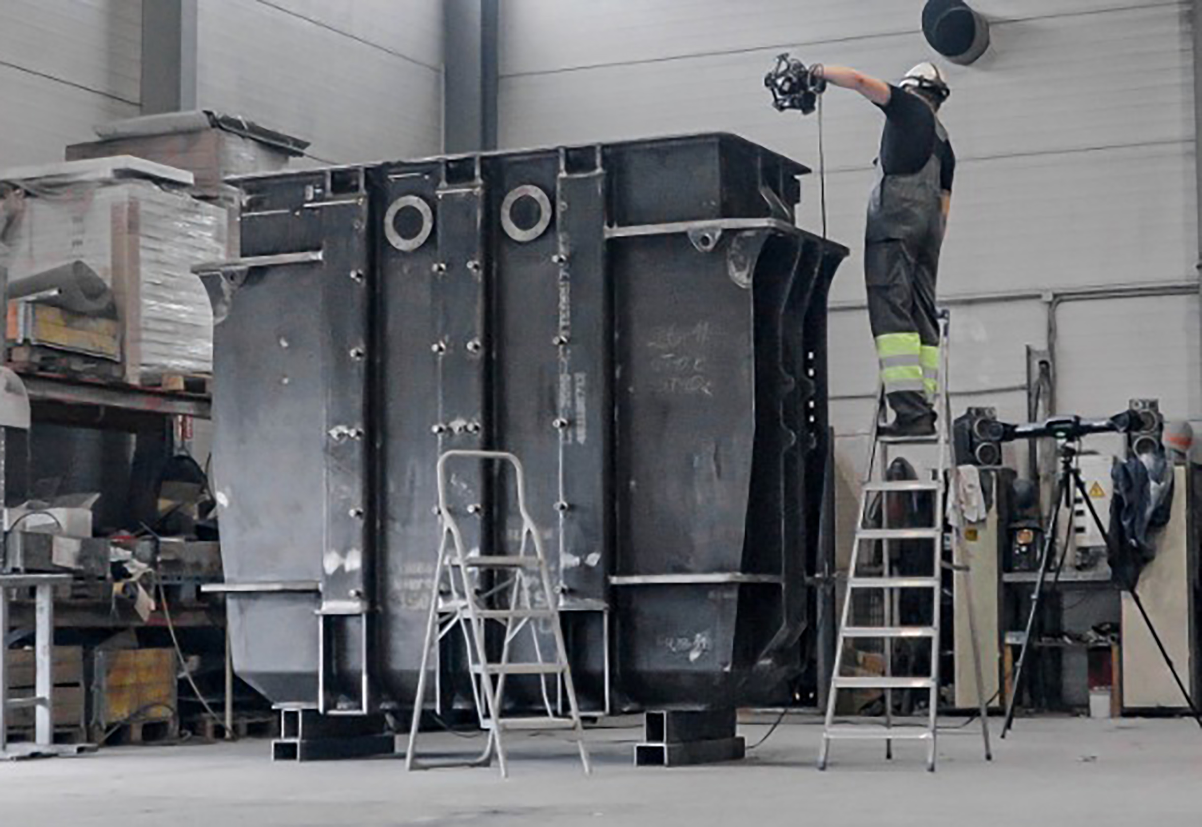 SFM employee on a ladder wearing a white helmet and a respirator, using a MetraSCAN 3D to scan a transformer tank
