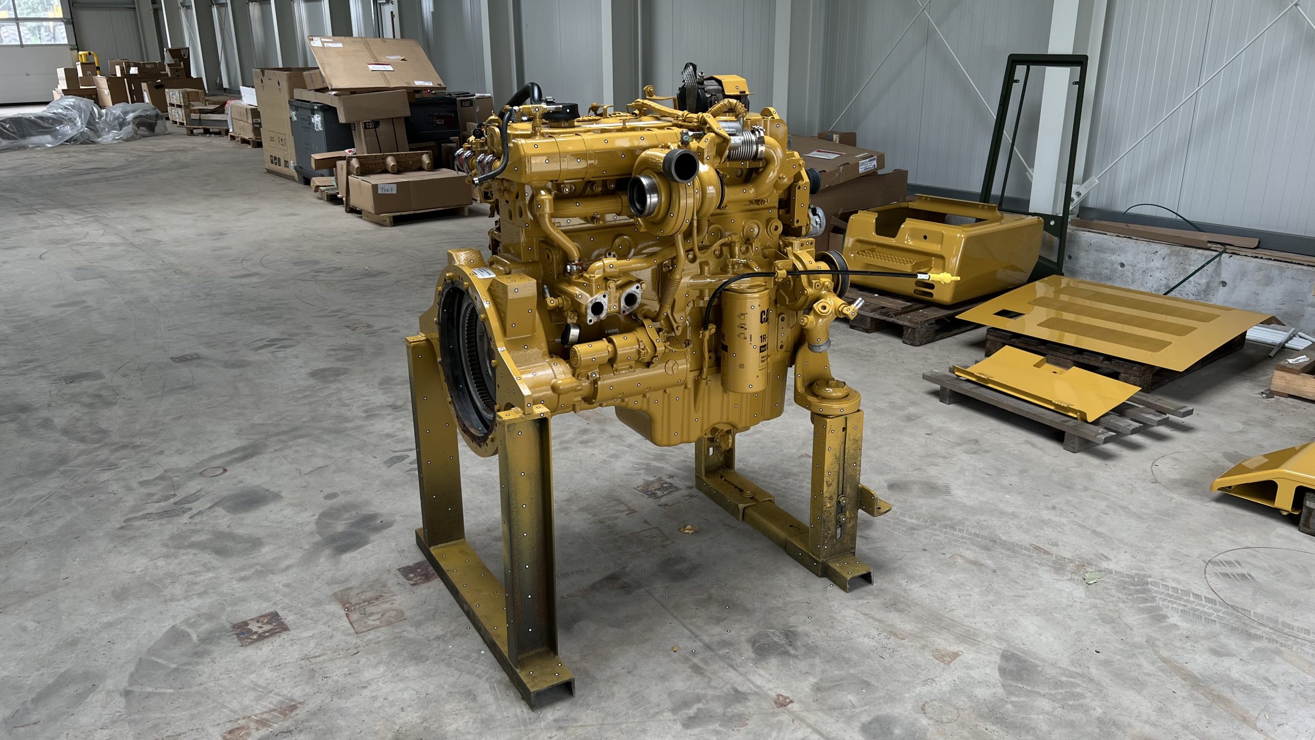 Gold-colored engine block on a trolley mount standing on the concrete floor of a hall. Cardboard boxes can be seen in the background.