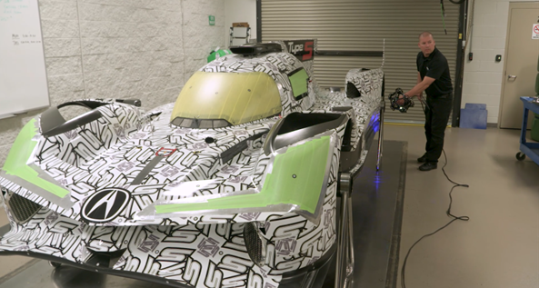 Employee using the MetraSCAN 3D scanner to measure the outside of a black and white race car in a shop