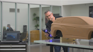 Employee using the HandySCAN BLACK to scan the clay model of the car next to a laptop displaying the scan data