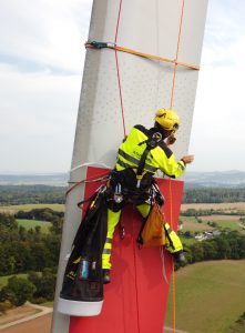 An employee anchored to a wind turbine blade with rope preparing it for the scan by applying targets