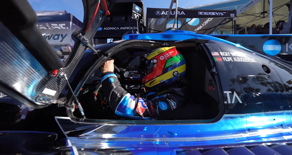Close up of a driver with a helmet through the open side door of a blue racing car