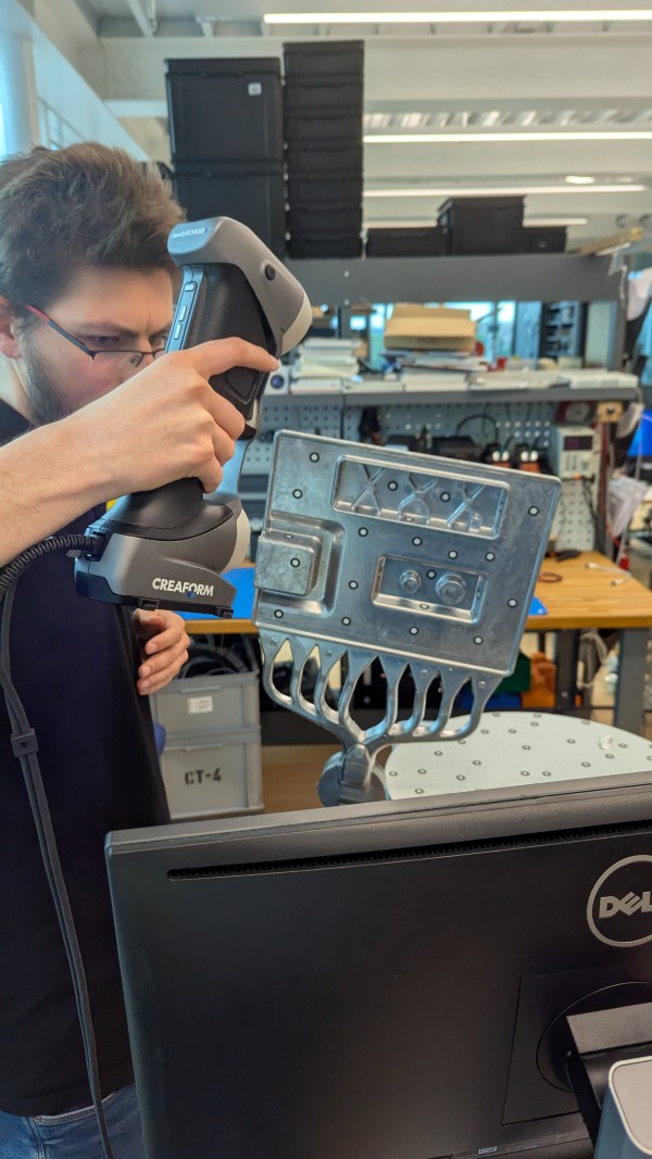 Mitarbeiter nutzt den HandySCAN 3D von FARO CREAFORM zur präzisen 3D Erfassung eines metallischen Bauteils im Werkstatt  und Prototyping Umfeld.