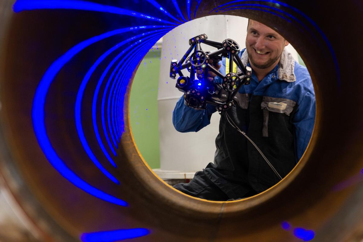 A man scans the inside of a pipe with MetraSCAN 3D. You can see the blue laser lines in the tube.